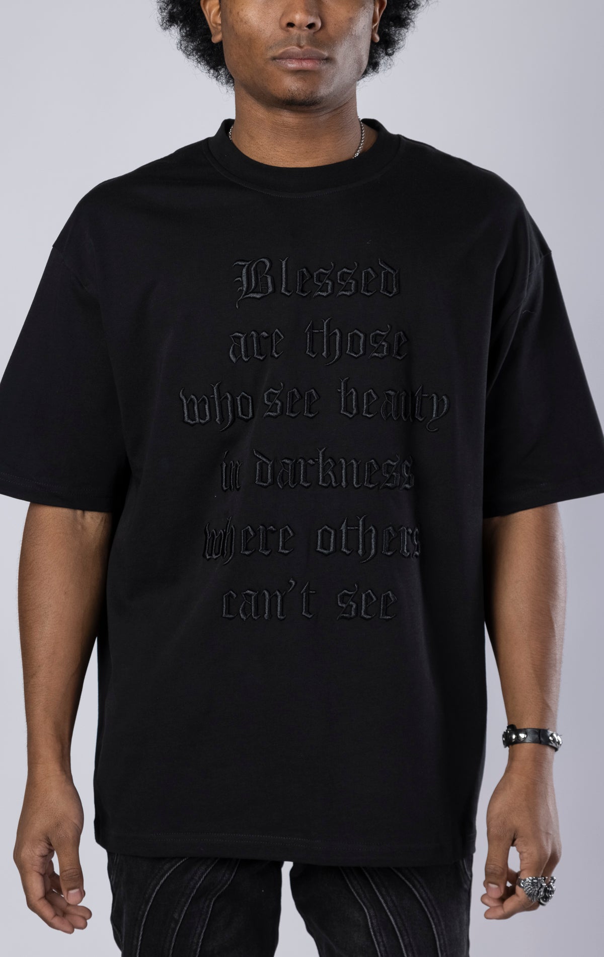 Blessed Darkness Boxy Tee. Black t-shirt made from 100% heavy black 250gr cotton. Features a boxy fit, dropped shoulders, longer sleeves, a 3D embroidered front message, and subtle "blessed" branding